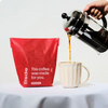 Person pouring coffee from a French press into a mug next to a red Trade coffee bag.