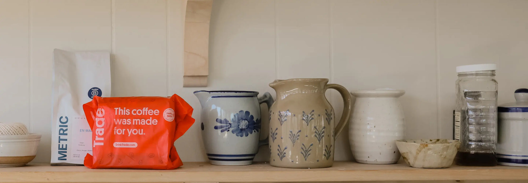 Kitchen shelf with ceramic jugs, a coffee bag, and a red Trade bag that reads "This coffee was made for you."