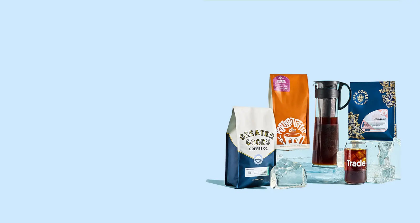 Bags of cold brew, a cold brewer, and a glass of cold brew displayed over large ice cubes