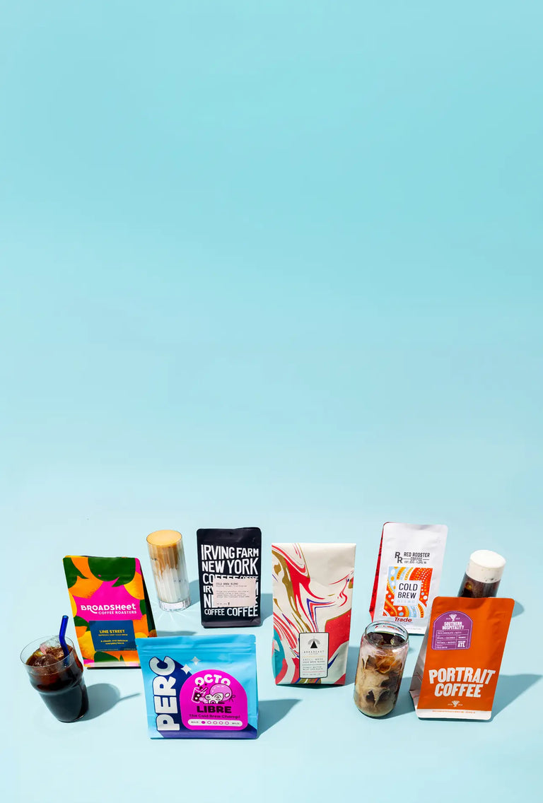 Bags of cold brew, a cold brewer, and a glass of cold brew displayed over large ice cubes