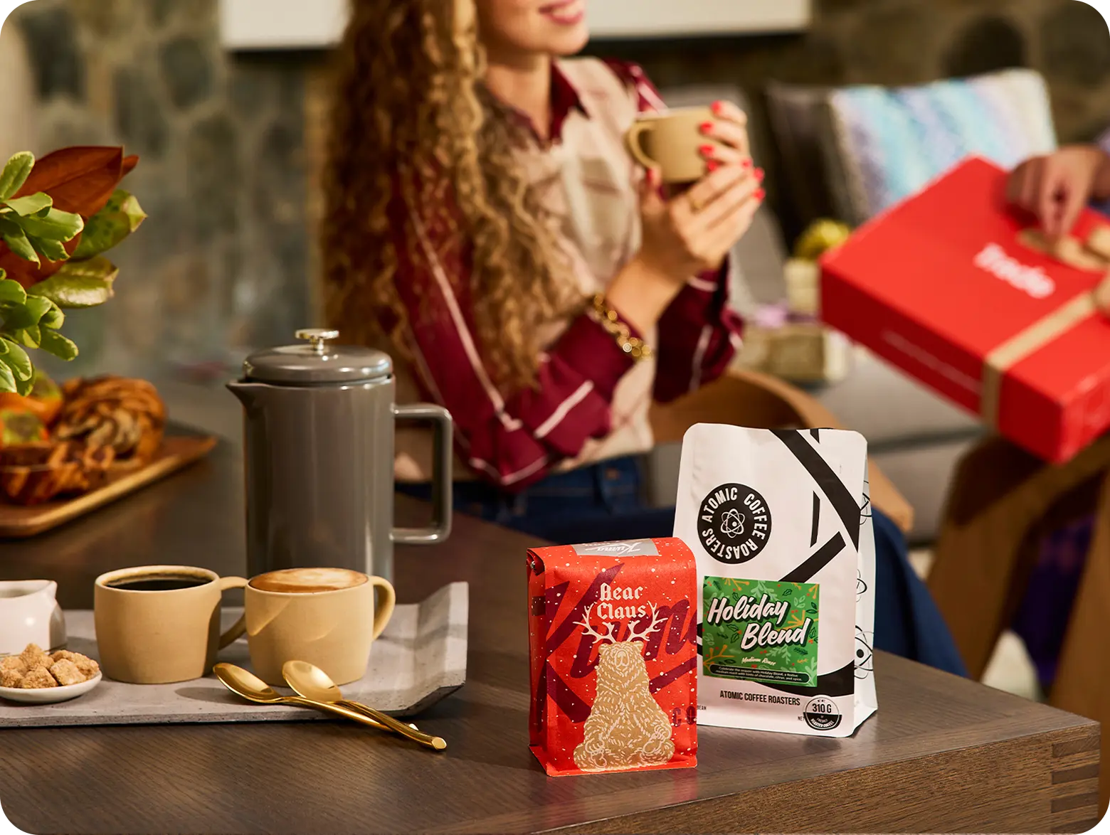 A variety of coffee bags from several different roasters along with a mug of coffee, all in front of a red Trade gift box.