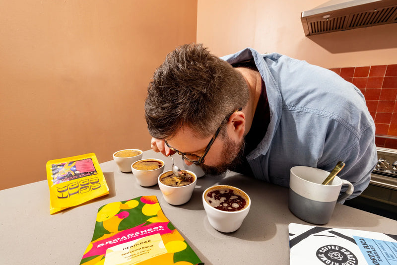 Man smelling a cup of coffee at a tasting table with coffee bags
