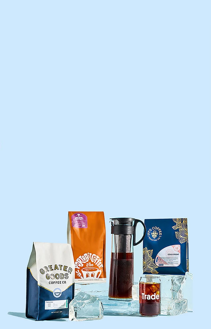 Bags of cold brew, a cold brewer, and a glass of cold brew displayed over large ice cubes